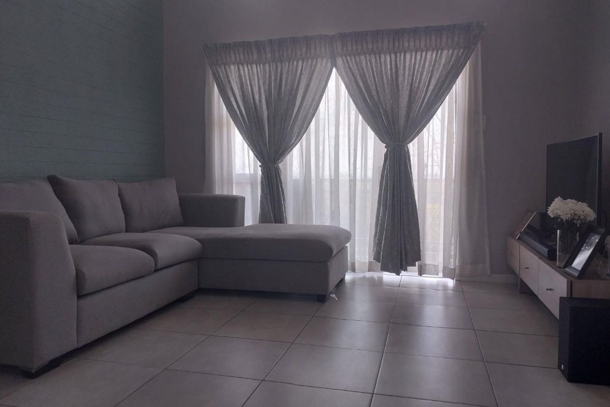 A comfortable living room featuring neutral tiled flooring, a textured feature wall, and large sliding glass doors that provide natural light.