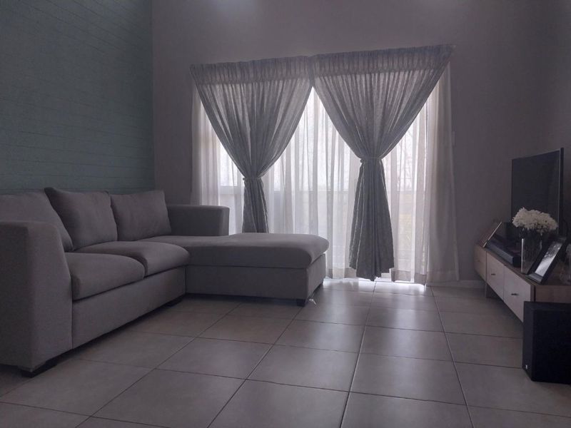 A comfortable living room featuring neutral tiled flooring, a textured feature wall, and large sliding glass doors that provide natural light.