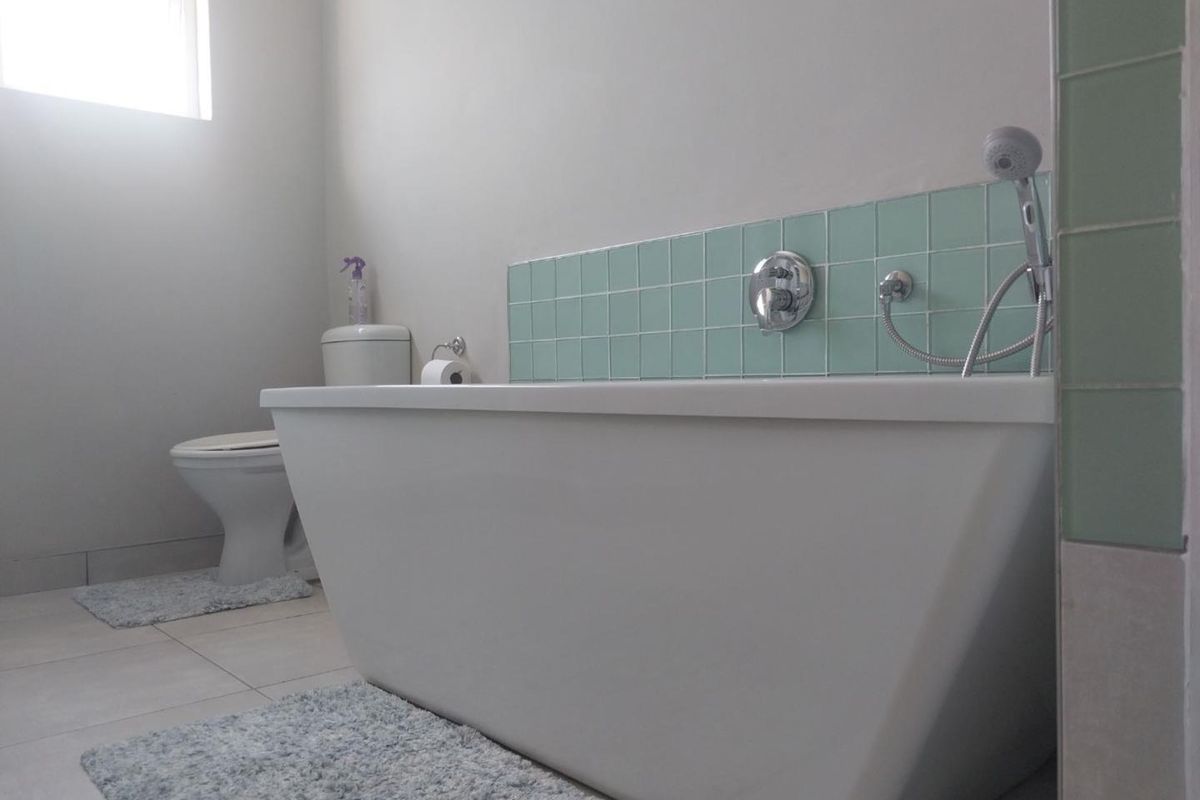 A clean bathroom featuring a modern freestanding bathtub with a wall-mounted shower mixer and a ceramic toilet.
