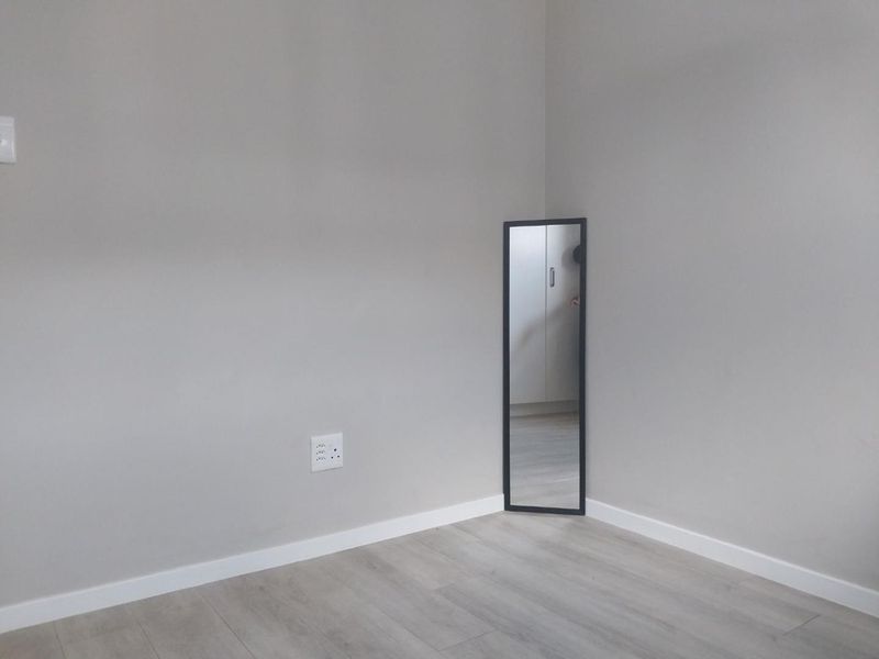 A clean, empty bedroom corner featuring light-toned laminate flooring, neutral wall paint, and modern skirting boards.