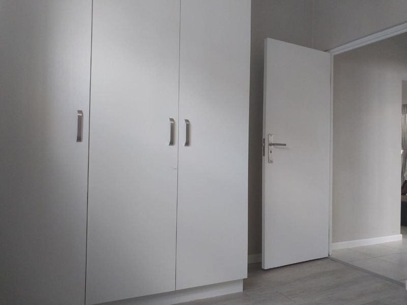 A clean, minimalist bedroom space featuring modern white built-in cupboards and light-toned laminate flooring, presenting a neutral canvas for interior design.