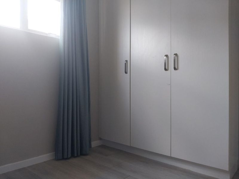 A clean, empty bedroom featuring modern laminate flooring and neutral-toned built-in cupboards with contemporary hardware.