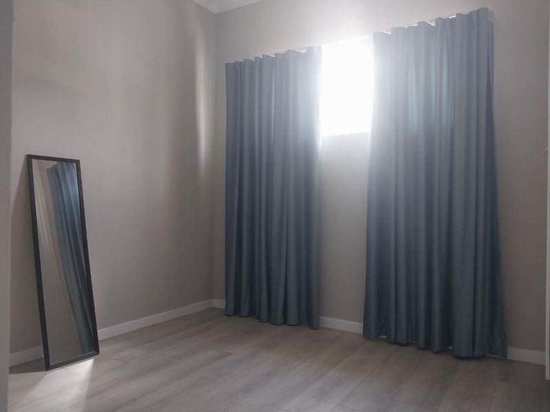 A bright, empty bedroom featuring neutral wall tones and modern laminate flooring, ready for personalization.