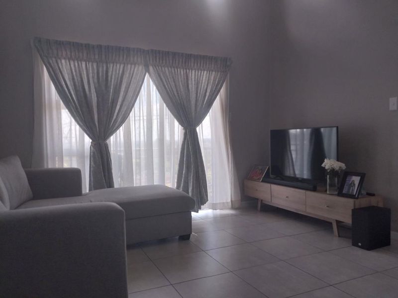 A comfortable living room featuring neutral tiled flooring and a large sliding glass door that provides natural light and access to the outdoors.