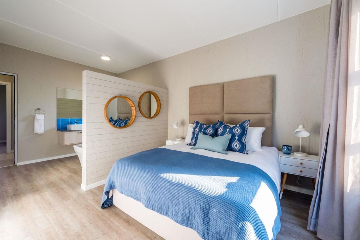 A modern bedroom featuring a semi-open plan layout with an integrated vanity area, neutral wall finishes, and durable laminate flooring.