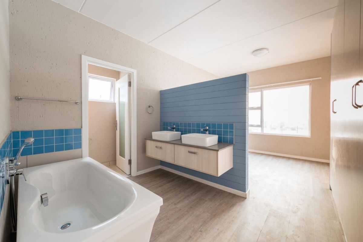 Spacious open-plan bathroom featuring a double vanity with vessel sinks, a built-in bathtub, and a modern blue partition wall.
