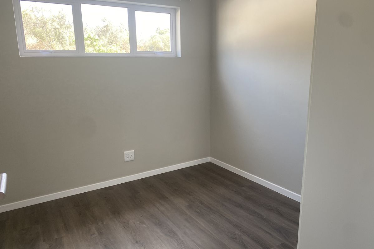 A clean, empty bedroom featuring modern laminate flooring, neutral wall paint, and a high-set window with a curtain rod.