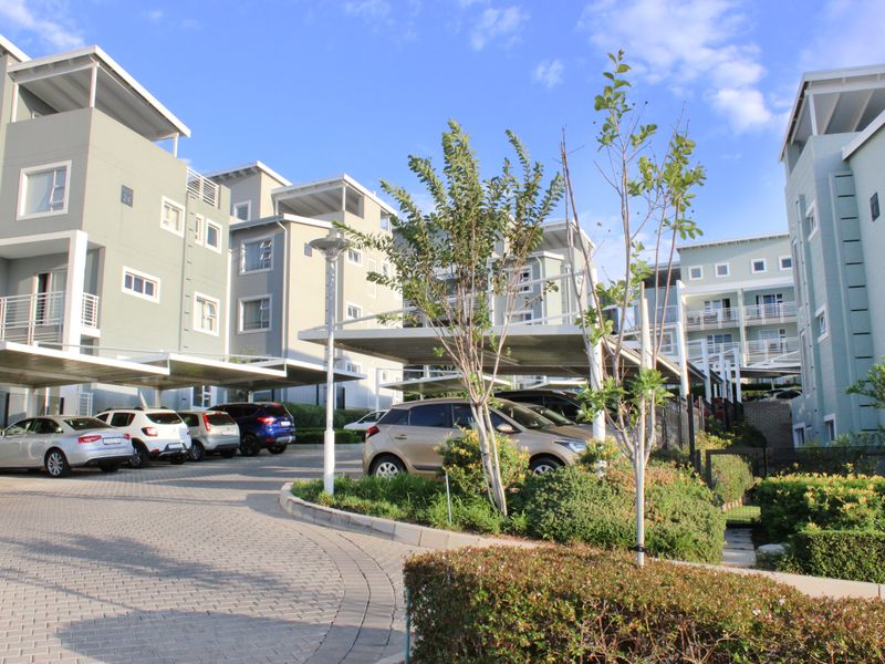 Exterior view of a modern apartment complex featuring paved driveways, covered parking carports, and well-maintained landscaped garden areas.