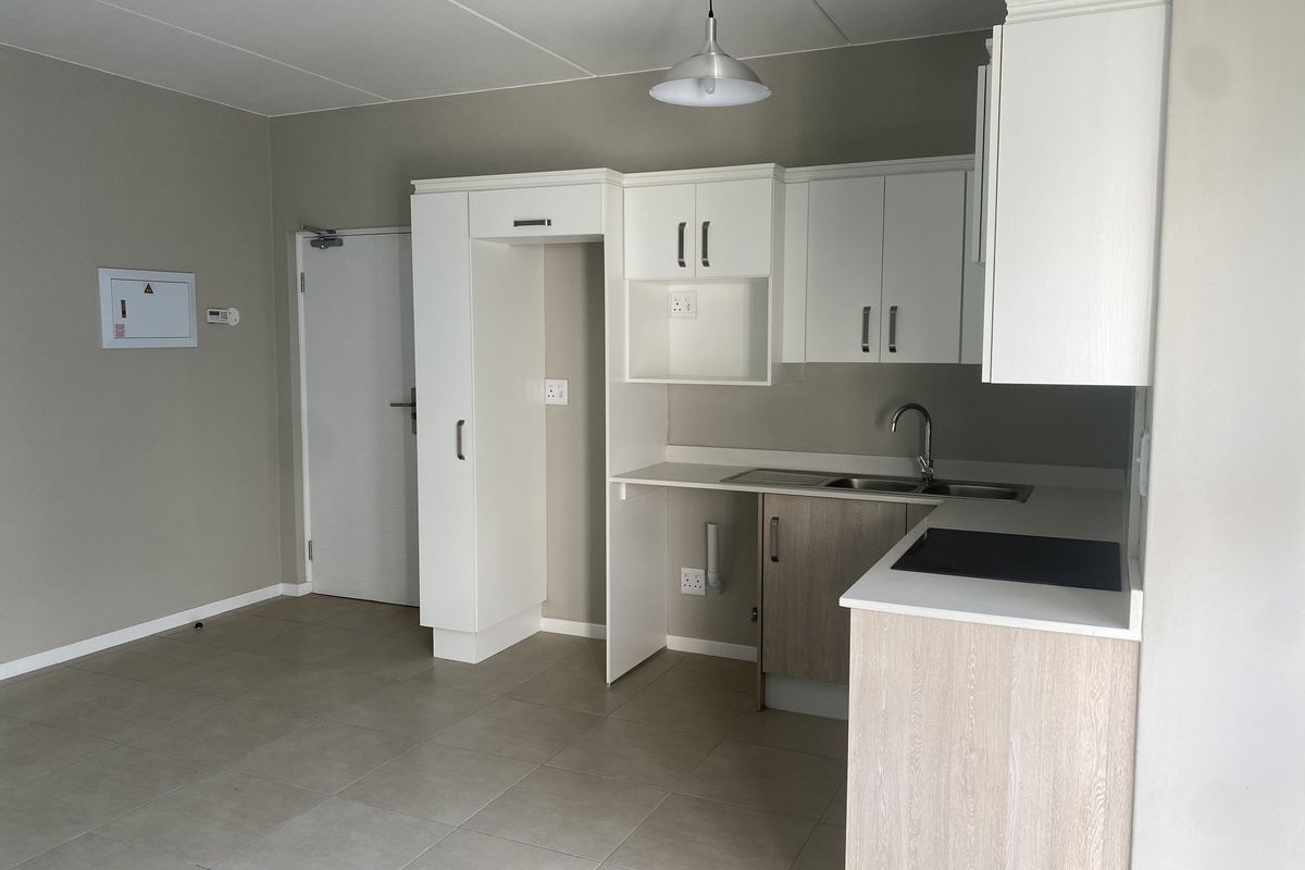 A clean, modern kitchen featuring neutral cabinetry, laminate countertops, a built-in hob, and tiled flooring in an open-plan layout.