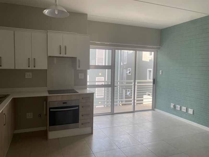 Open-plan living area featuring a modern kitchen with built-in oven and hob, tiled floors, and a sliding door leading to a balcony.