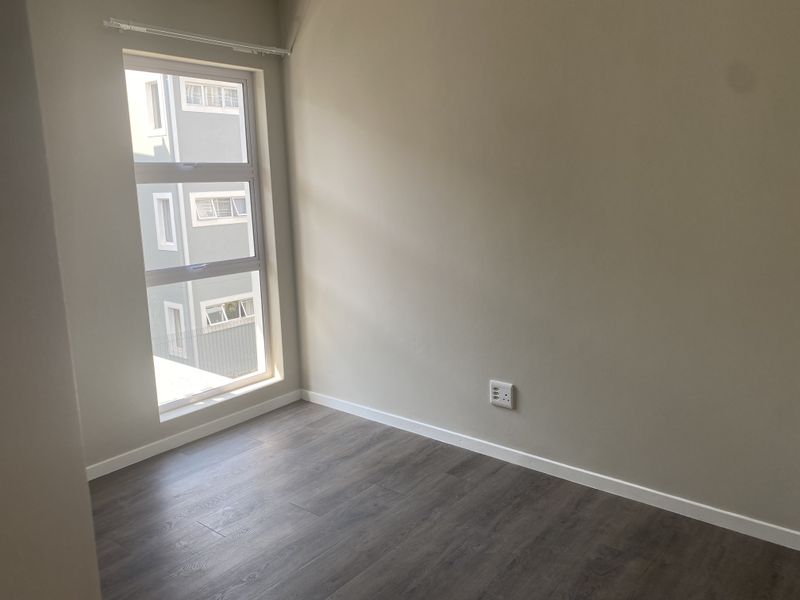 A clean, empty bedroom featuring modern laminate flooring, neutral wall paint, and an aluminium window frame with a curtain track.