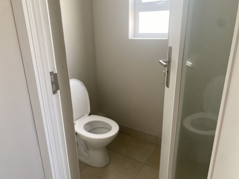A clean and functional guest bathroom featuring a toilet, tiled flooring, and a frosted glass door for privacy.