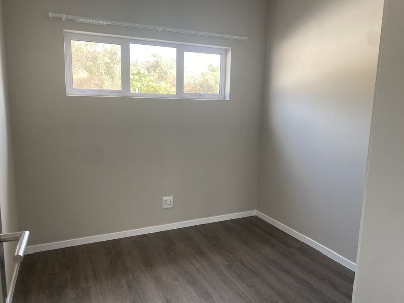 A clean, empty bedroom featuring neutral wall paint, modern laminate flooring, and a horizontal window with a fitted curtain rod.