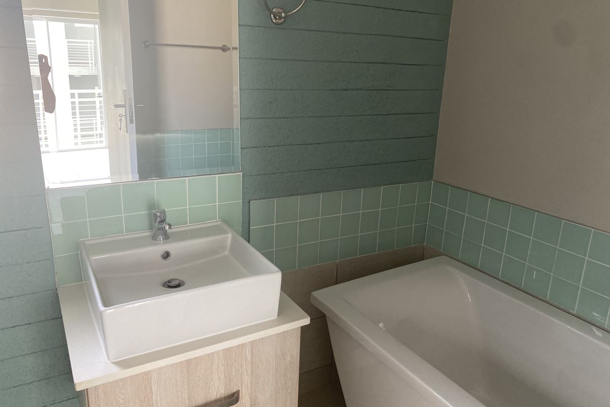 A clean bathroom featuring a modern vanity with a ceramic basin, a bathtub, and decorative green tiled wall accents.