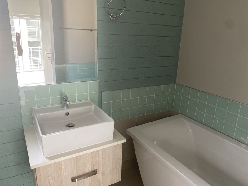 A clean bathroom featuring a modern vanity with a ceramic basin, a bathtub, and decorative green tiled wall accents.
