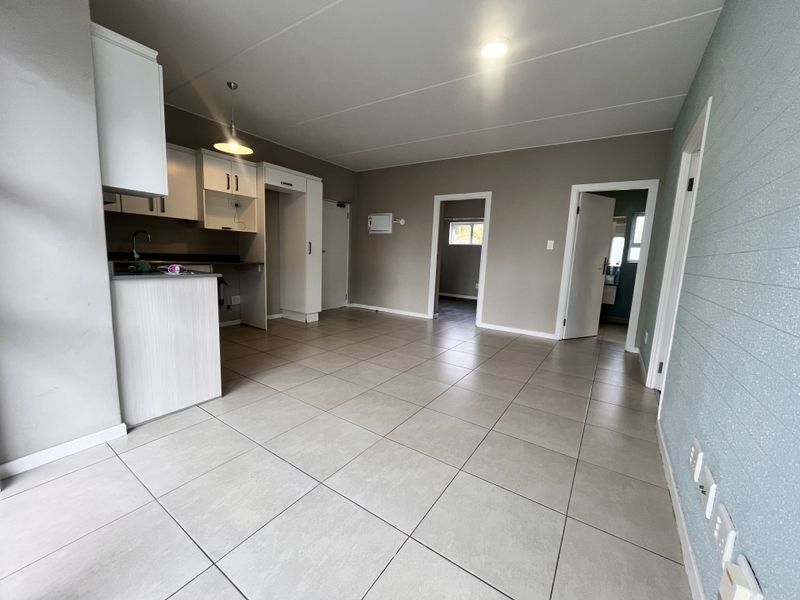 Spacious open-plan living area featuring tiled flooring, neutral walls, and a functional kitchen layout with built-in cabinetry and modern lighting.