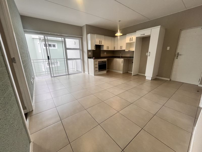 Open-plan living area featuring a modern kitchen with built-in cabinetry, oven, and hob, leading directly to a private balcony through sliding glass doors.