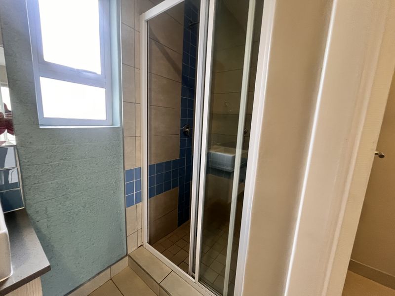 A functional bathroom featuring a shower enclosure with tiled walls, a vanity basin, and a window for natural light.