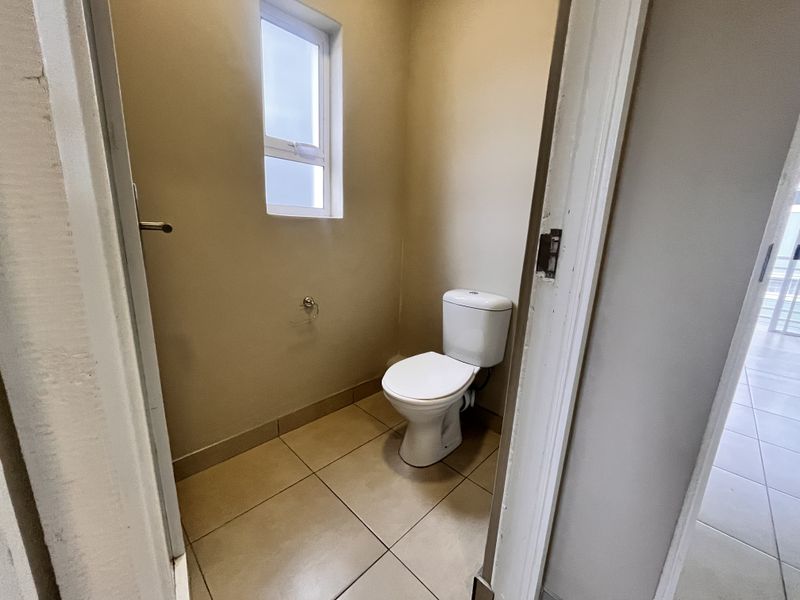 A compact, functional guest toilet featuring tiled flooring and a window for natural light.