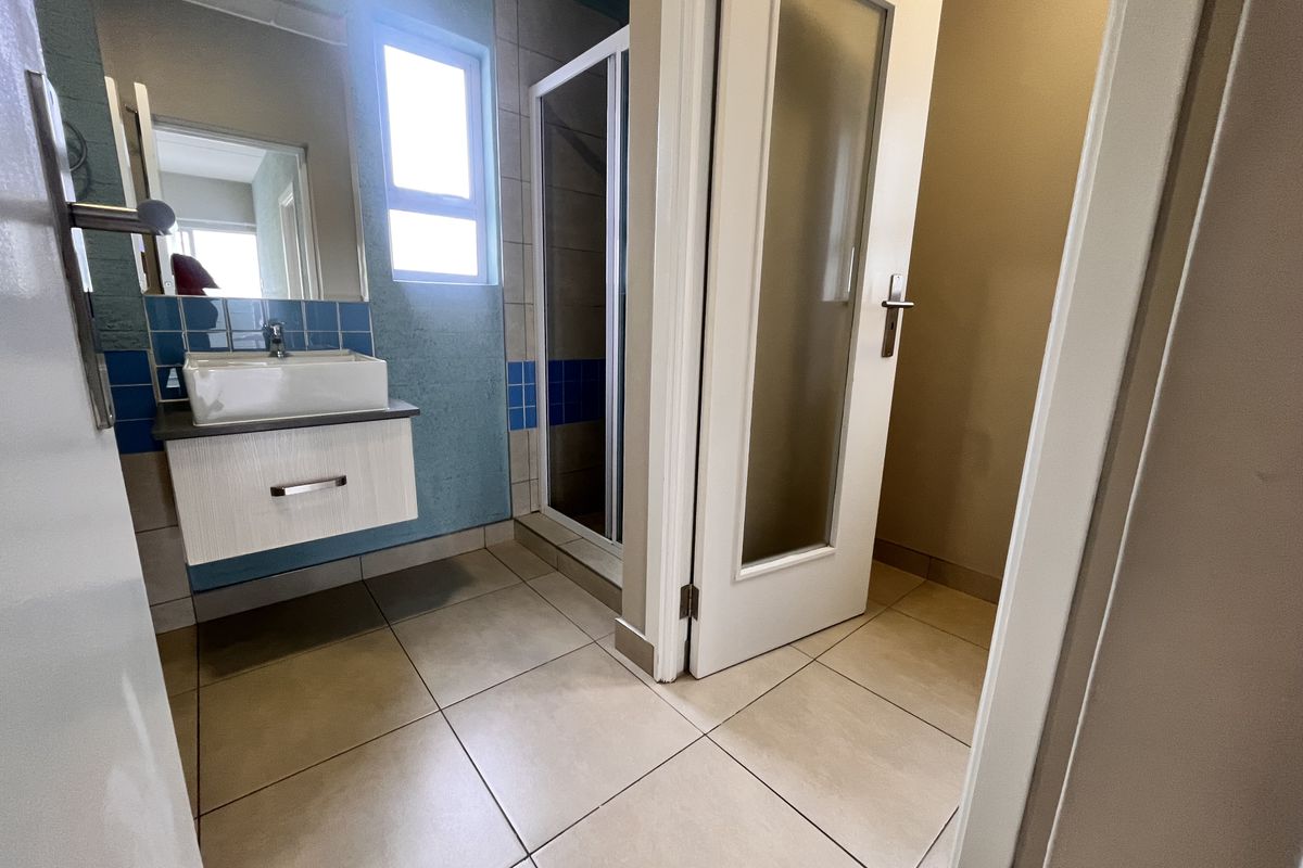 A functional bathroom featuring a wall-mounted vanity with a vessel sink, a separate shower enclosure, and neutral floor tiling.