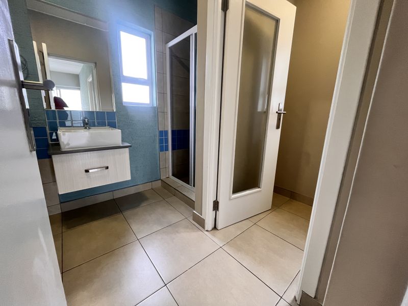 A functional bathroom featuring a wall-mounted vanity with a vessel sink, a separate shower enclosure, and neutral floor tiling.