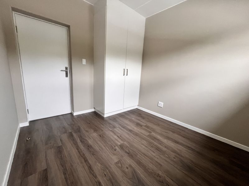 A clean, empty bedroom featuring modern laminate flooring, neutral wall tones, and a built-in white wardrobe.