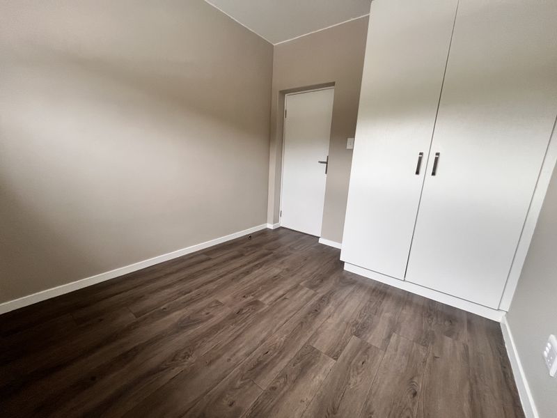 A clean, empty bedroom featuring modern laminate flooring, neutral wall tones, and a built-in white wardrobe.