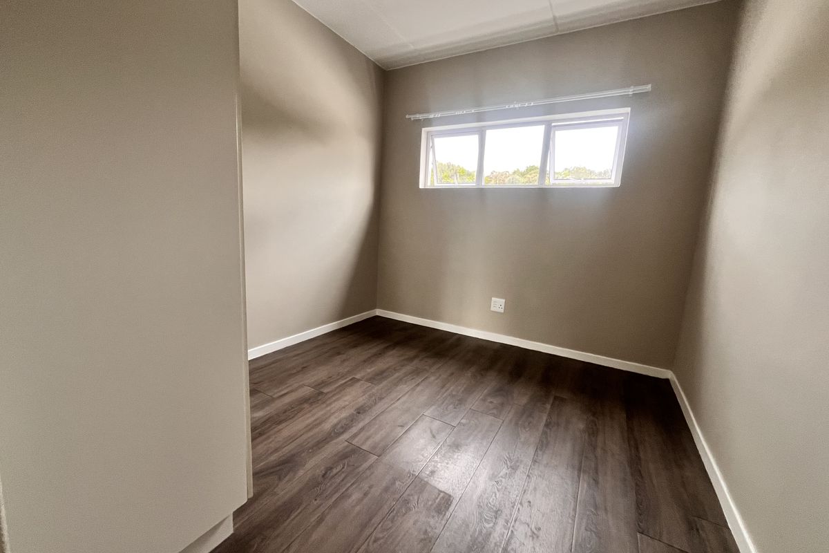 A clean, empty bedroom featuring modern dark laminate flooring, neutral wall paint, and a top-hung window providing natural light.