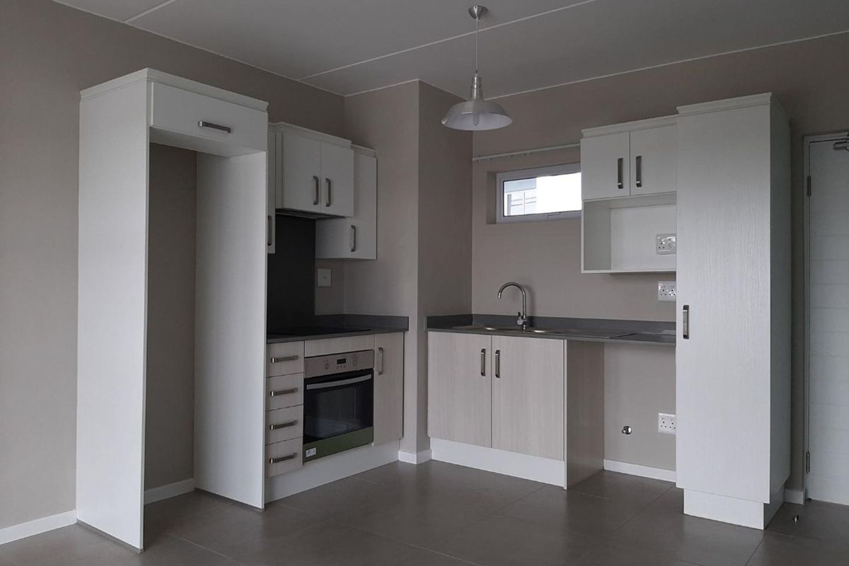 A clean, modern kitchen featuring built-in cabinetry, an integrated oven, a sink, and neutral tiled flooring in an open-plan layout.