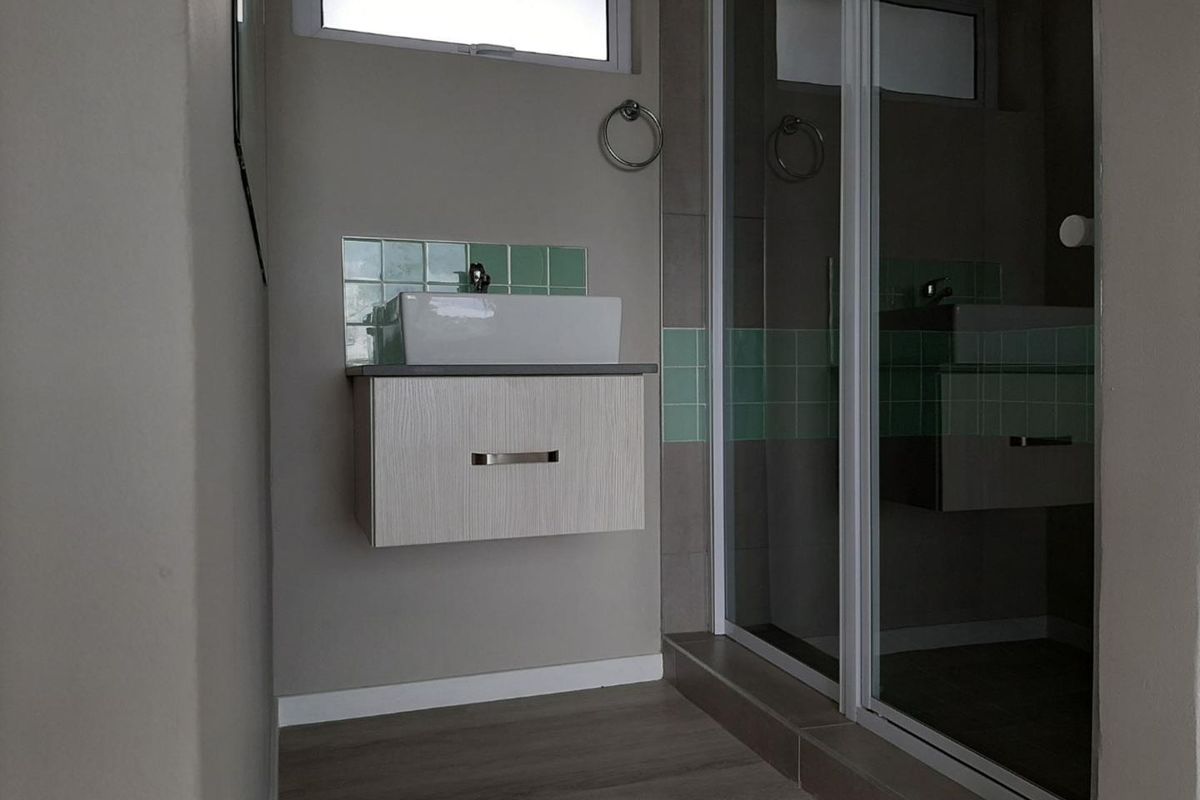 A modern bathroom featuring a wall-mounted vanity with a vessel sink, tiled splashback, and a glass-enclosed shower.