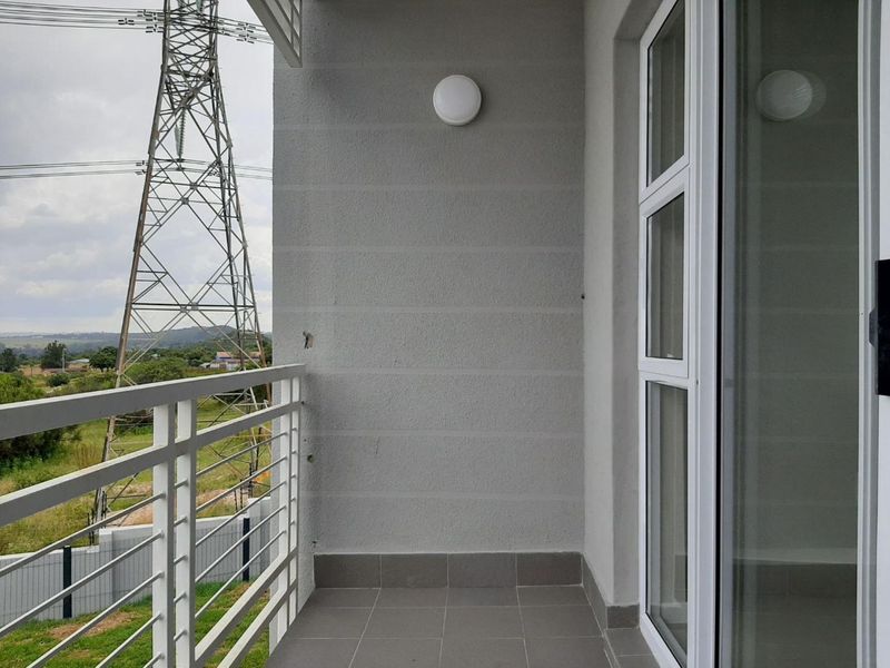 A clean, modern balcony featuring tiled flooring, a white metal balustrade, and a sliding glass door entrance.