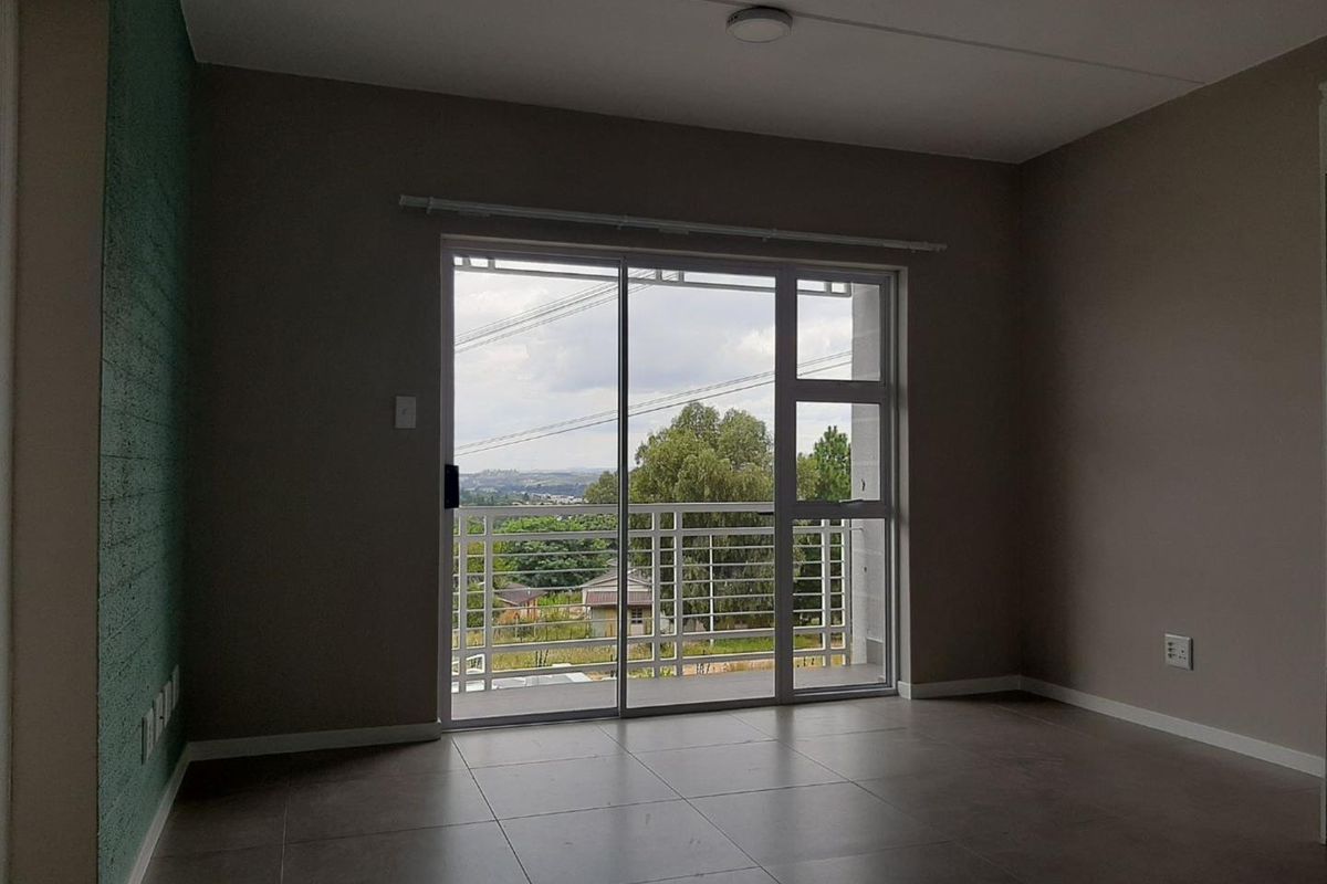 An empty living room featuring large sliding glass doors that open onto a balcony with scenic views and modern tiled flooring.