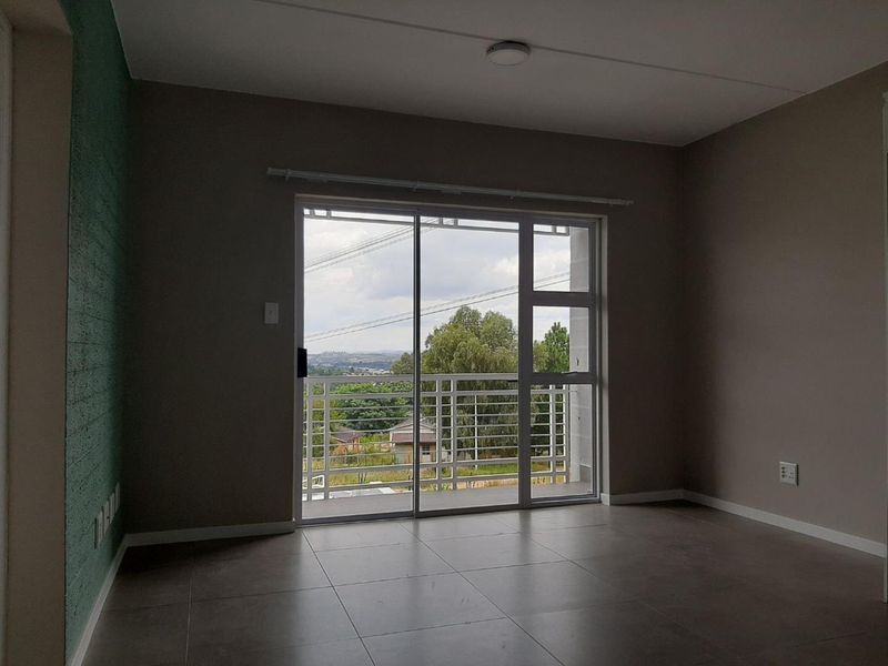 An empty living room featuring large sliding glass doors that open onto a balcony with scenic views and modern tiled flooring.