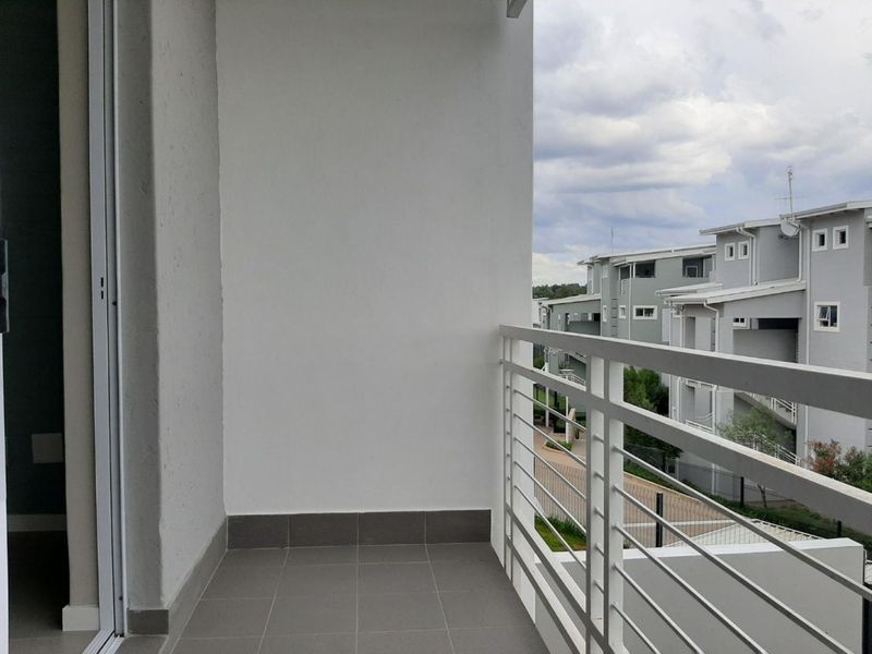 A clean, modern balcony featuring tiled flooring and a white metal balustrade, offering an open outdoor space with views of the surrounding apartment complex.