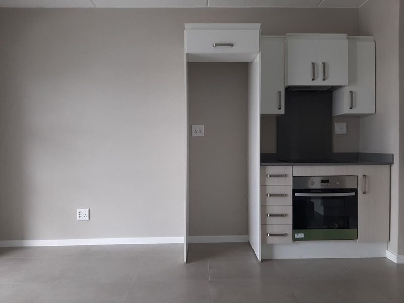 A clean, modern kitchen featuring built-in cabinetry, an integrated oven, hob, and extractor fan, with neutral tiled flooring and a dedicated refrigerator alcove.