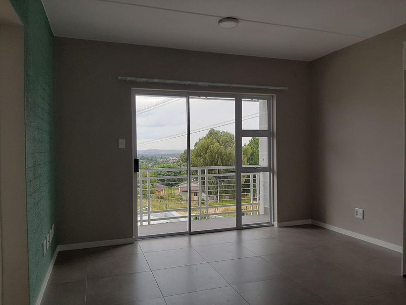 An empty living room featuring large sliding glass doors that open onto a balcony with scenic views and modern tiled flooring.