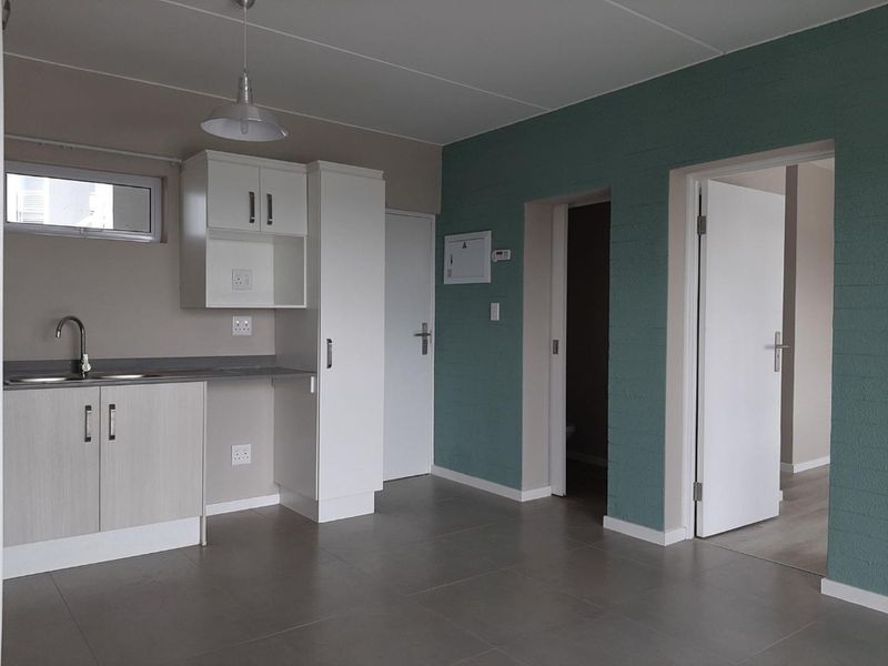 A clean, modern kitchen area featuring neutral cabinetry, tiled flooring, and direct access to adjacent rooms, presenting a well-maintained and functional space.