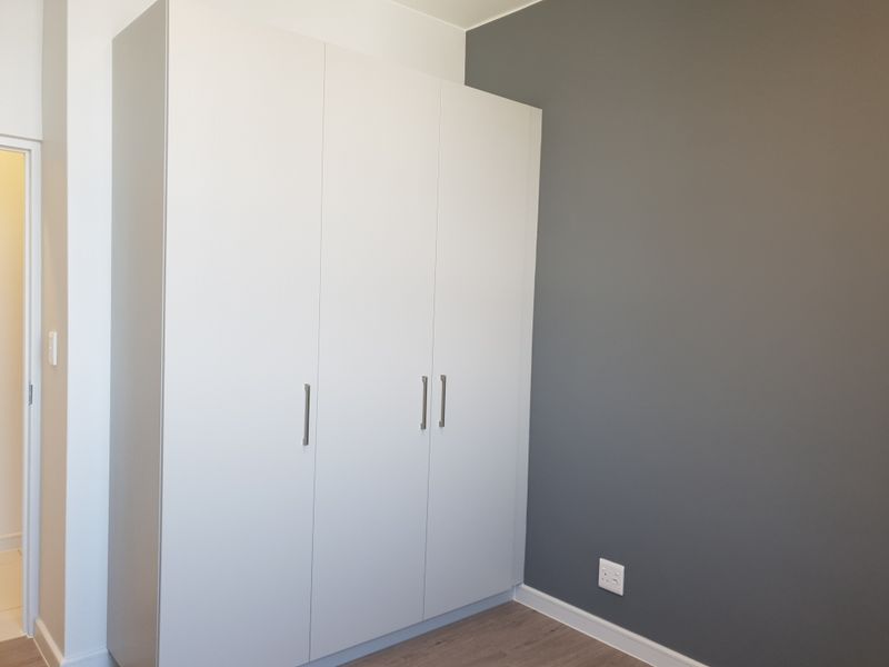 A clean, empty bedroom featuring modern built-in wardrobes, laminate flooring, and a contrasting grey accent wall.