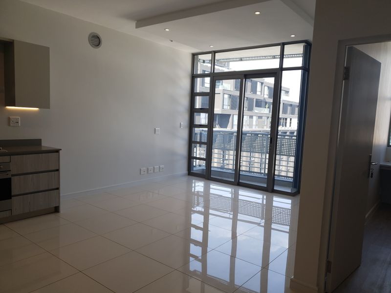 Modern open-plan living area featuring polished tile flooring, recessed lighting, and large sliding glass doors leading to a private balcony.