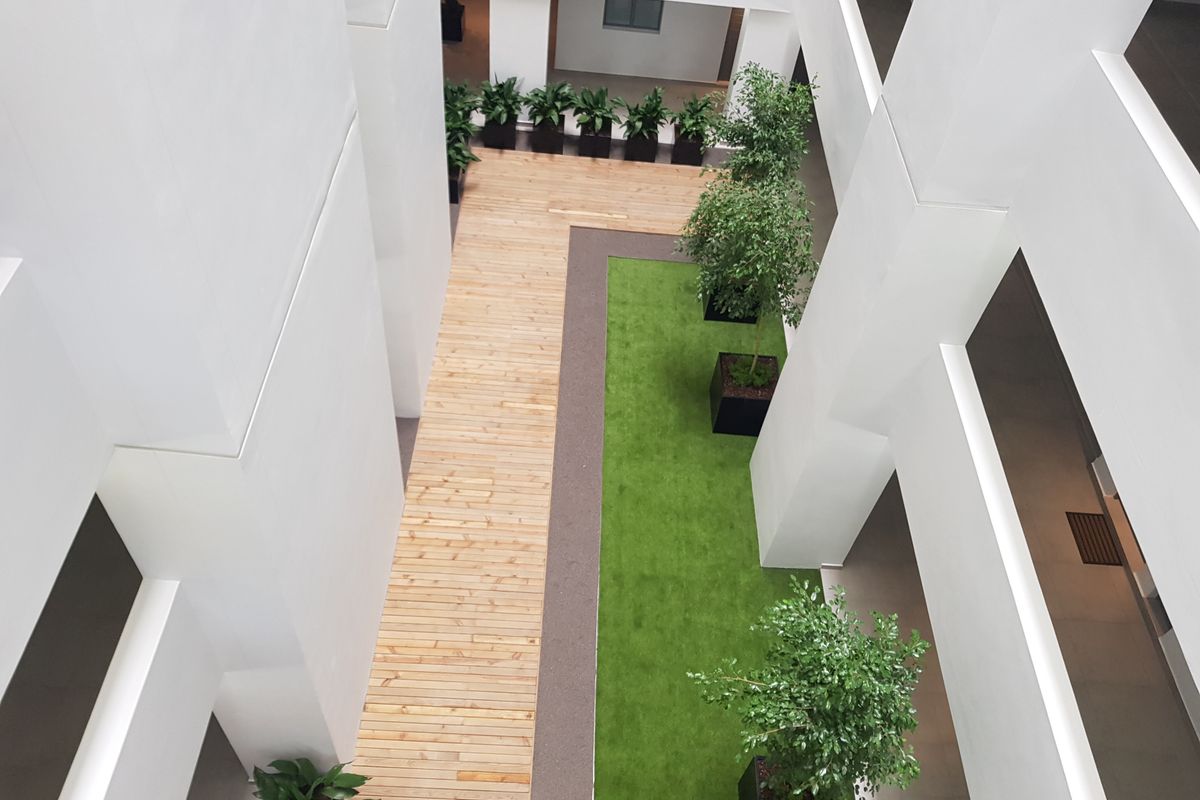 An elevated view of a modern apartment complex atrium featuring timber decking, artificial grass, and architectural white pillars.