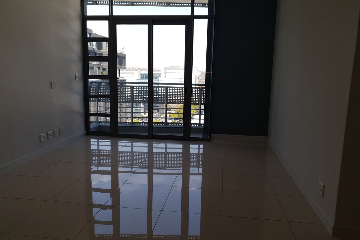 An empty, modern living area featuring polished tile floors and a large sliding glass door leading to a balcony with metal railings.