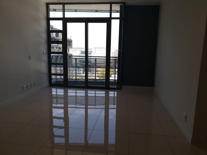 An empty, modern living area featuring polished tile floors and a large sliding glass door leading to a balcony with metal railings.