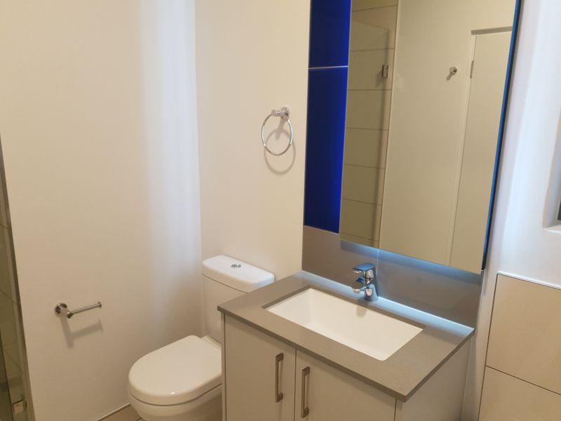 A clean and modern bathroom featuring a vanity with basin, wall-mounted mirror, and toilet.