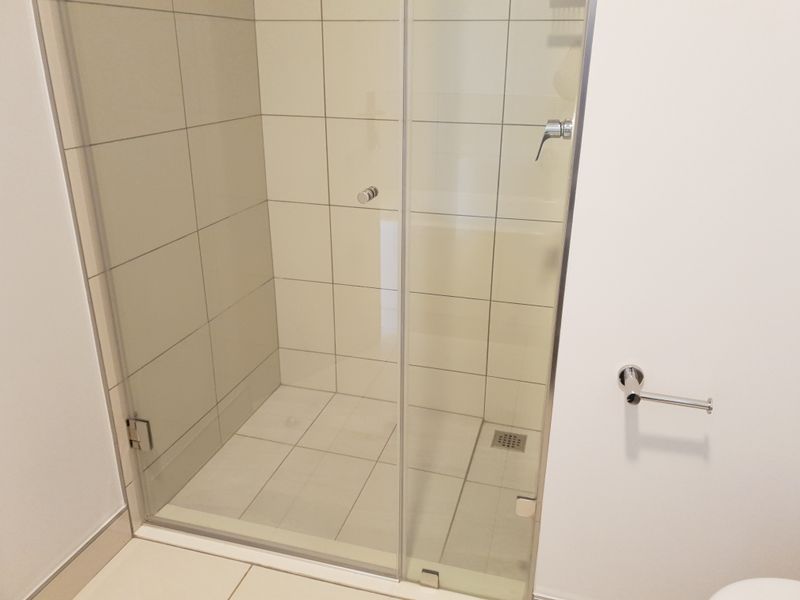 A clean, modern bathroom featuring a glass-enclosed walk-in shower with neutral wall and floor tiling.