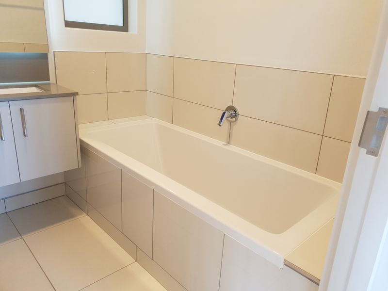 A clean, modern bathroom featuring a built-in bathtub with wall-mounted mixer, vanity cabinet, and neutral tiled finishes.