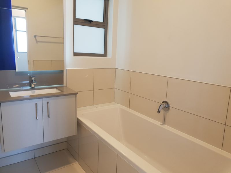A clean, modern bathroom featuring a vanity with basin, wall-mounted mirror, and a bathtub with tiled surround and wall finishes.