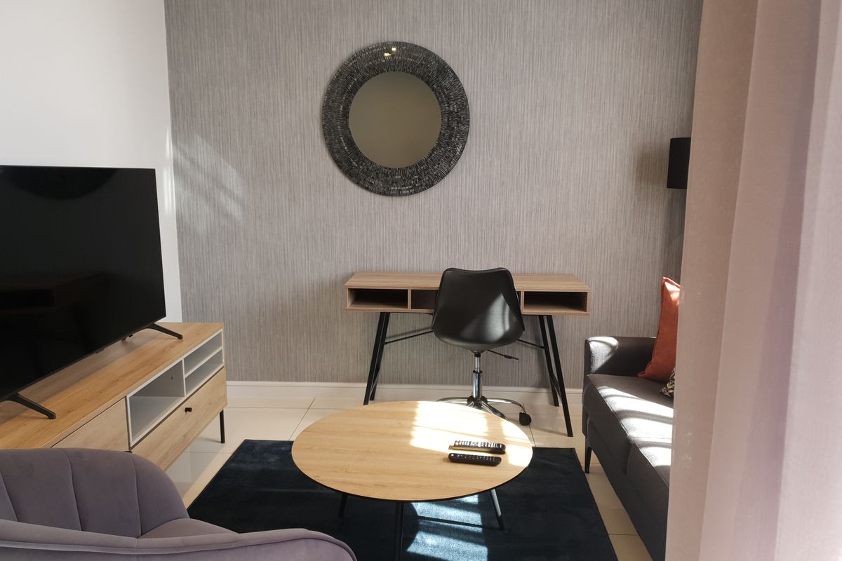 A well-maintained living room featuring neutral textured wallpaper, tiled flooring, and clean architectural lines, creating a bright and functional living space.