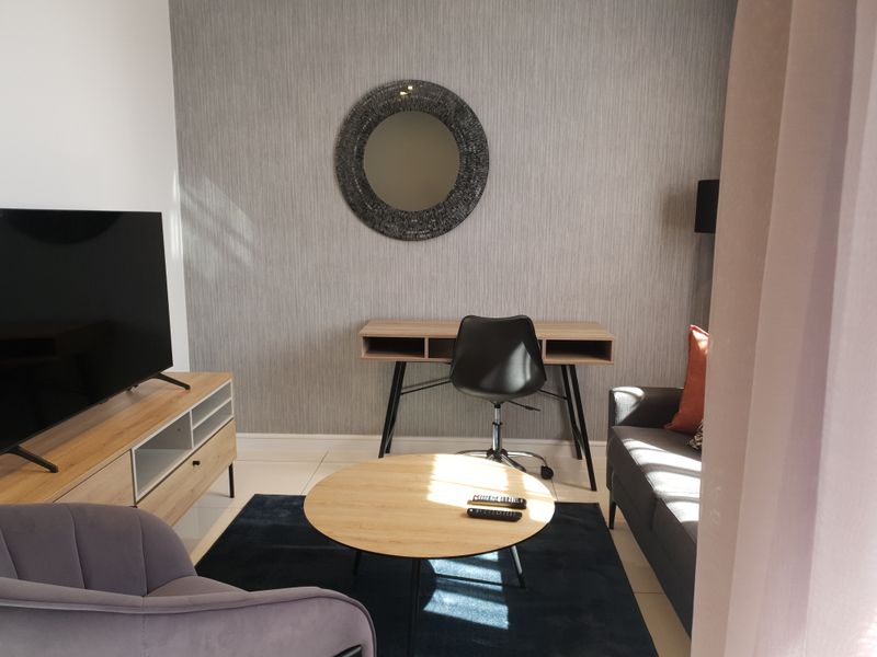 A well-maintained living room featuring neutral textured wallpaper, tiled flooring, and clean architectural lines, creating a bright and functional living space.