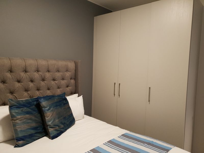 A well-maintained bedroom featuring a neutral-toned built-in wardrobe and a modern grey accent wall.