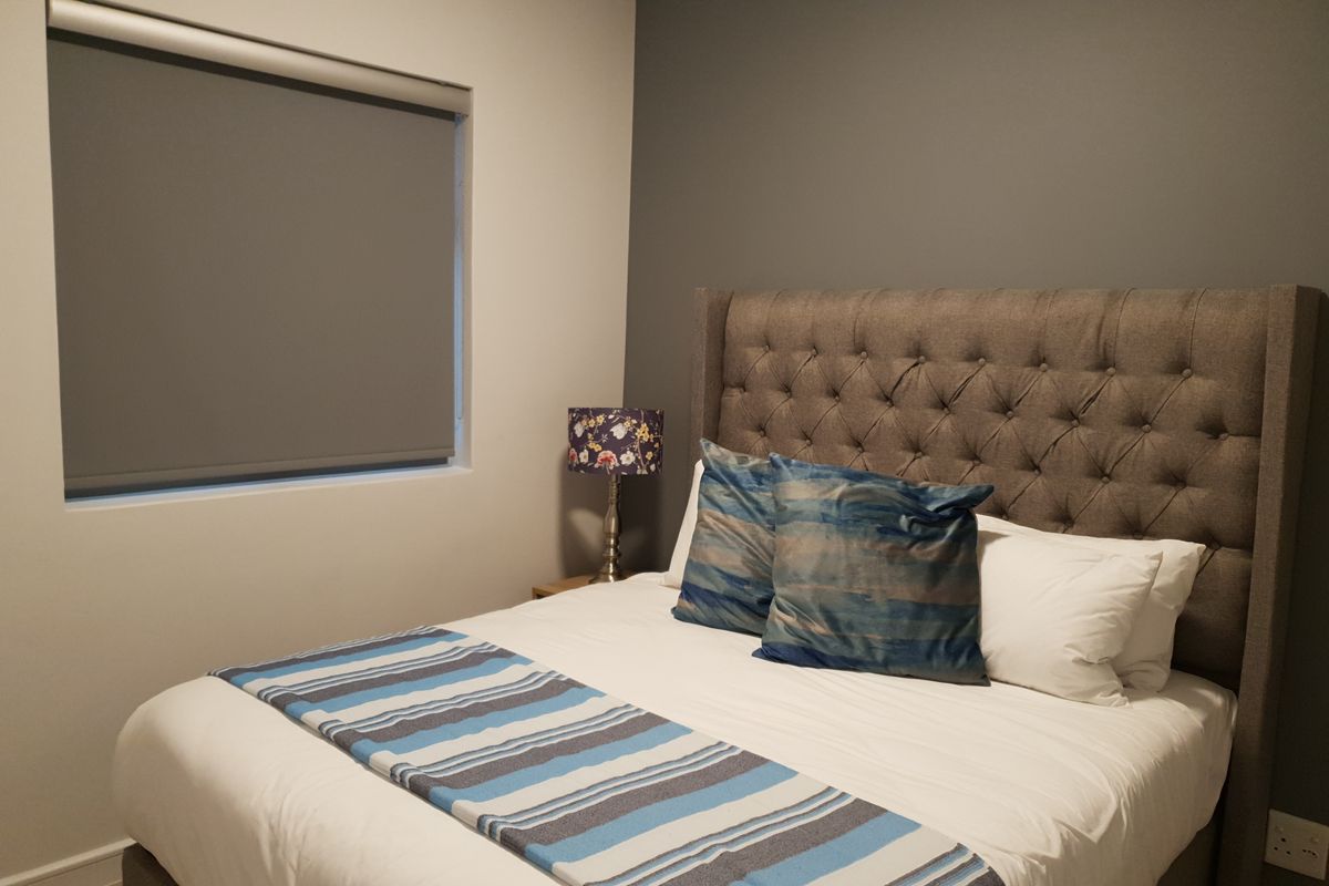 A well-maintained bedroom featuring a neutral color palette, an accent wall, and a fitted roller blind for privacy.